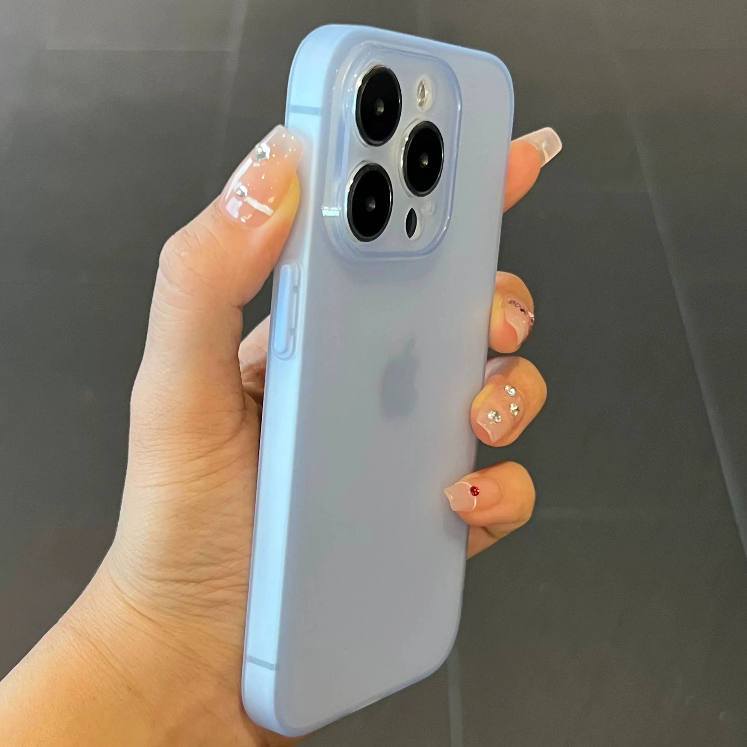 Hand holding a light blue phone case with a clear back on a dark background