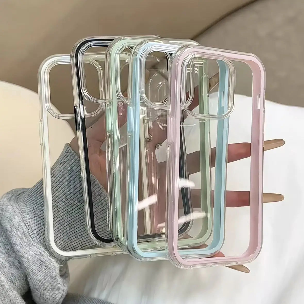Four clear phone cases in different colors held by a hand against a neutral background