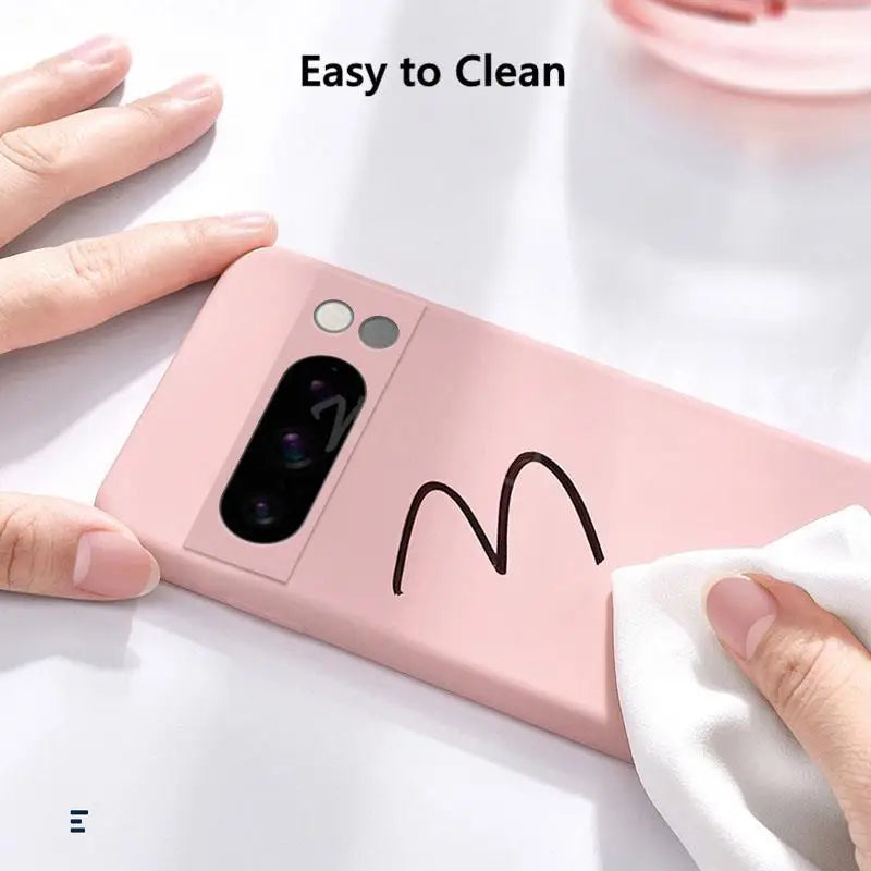 Pink phone case with a hand cleaning it using a white cloth on a light background.