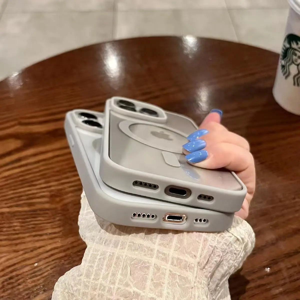 Person holding two phone cases on a wooden table in the background